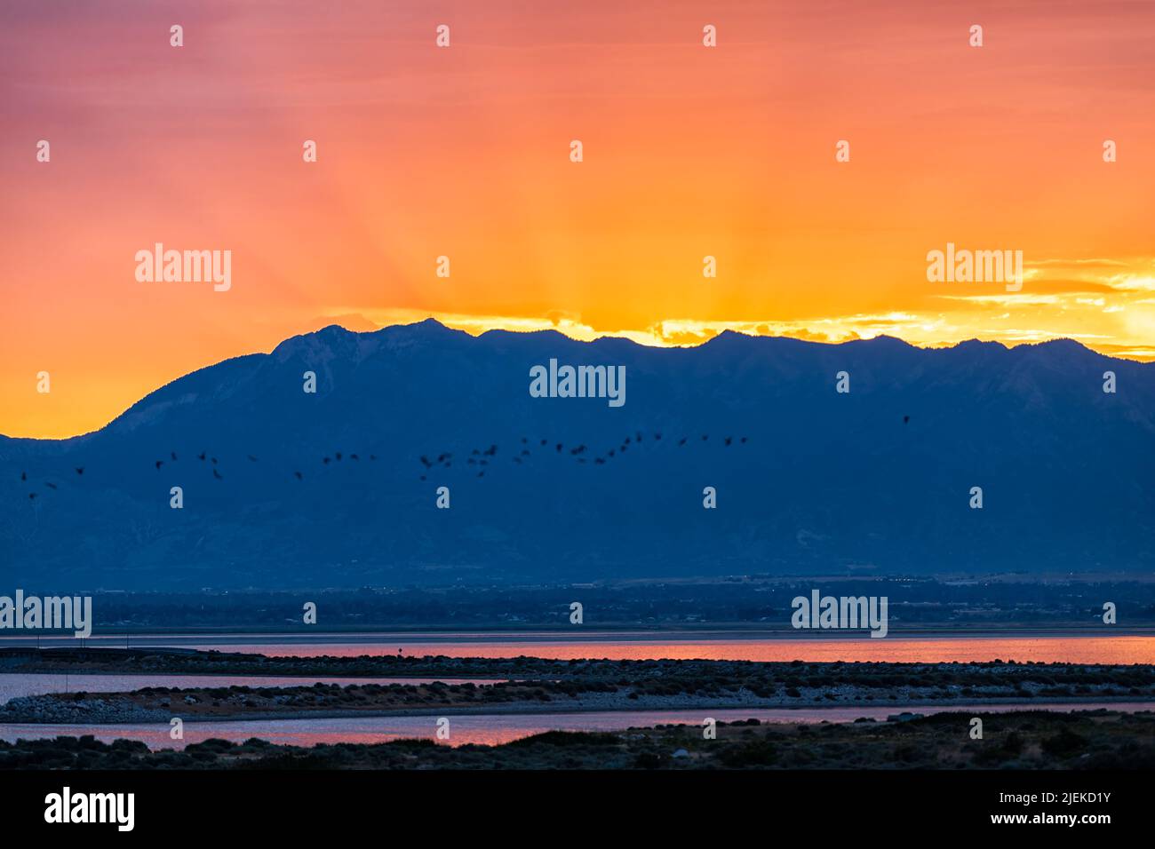 Orange red yellow sunlight sunrise on Great Salt Lake in Antelope Island State Park Ladyfinger campground with reflection on water and sun rays beams Stock Photo