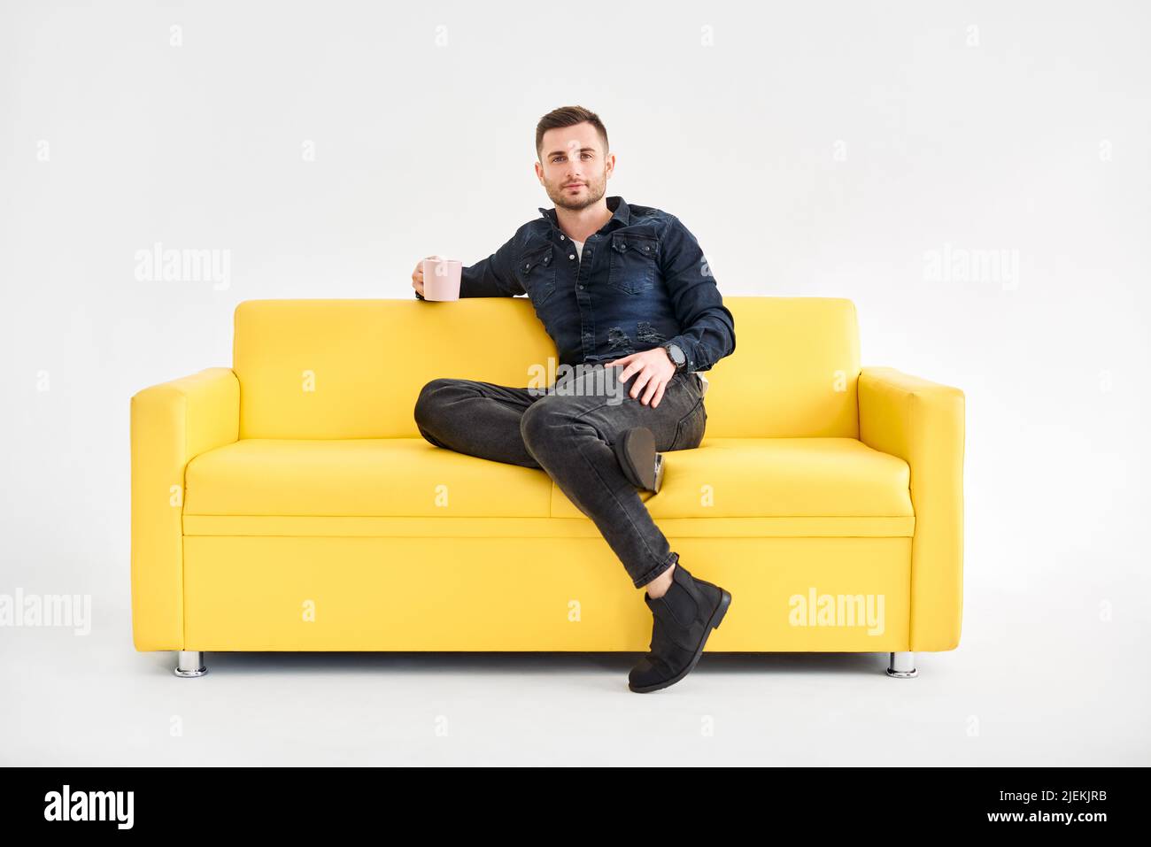 Relaxed man with coffee mug in hands sitting on comfort bright sofa looking to camera. good morning concept Stock Photo