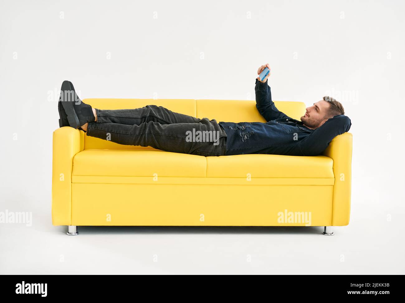 Relaxed man lying on yellow sofa talk on video call by his mobile phone over white background. Social media concept Stock Photo