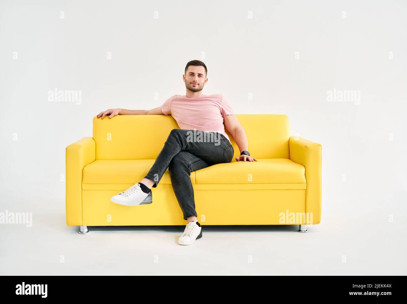 Handsome trendy man posing looking to camera while sitting on comfort sofa over white background. Male portrait Stock Photo