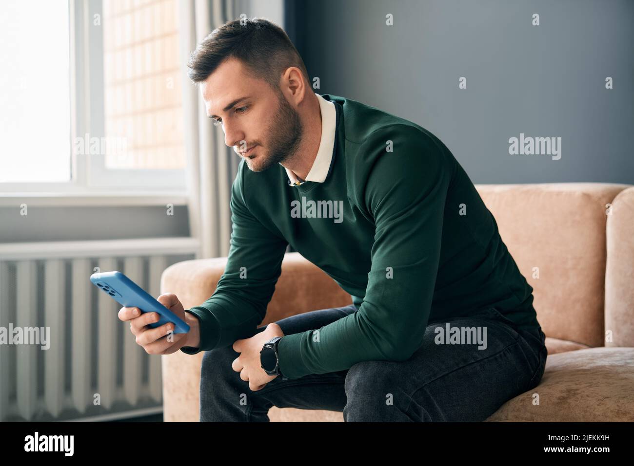 Relaxed man sitting on couch using hsi mobile smart phone at home. Social media concept Stock Photo
