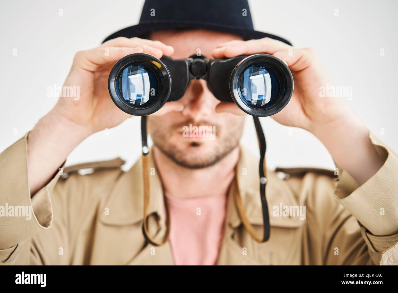 Young man wearing in coat and hat looking through binoculars over isolated white background. Spy,  espionage concept Stock Photo
