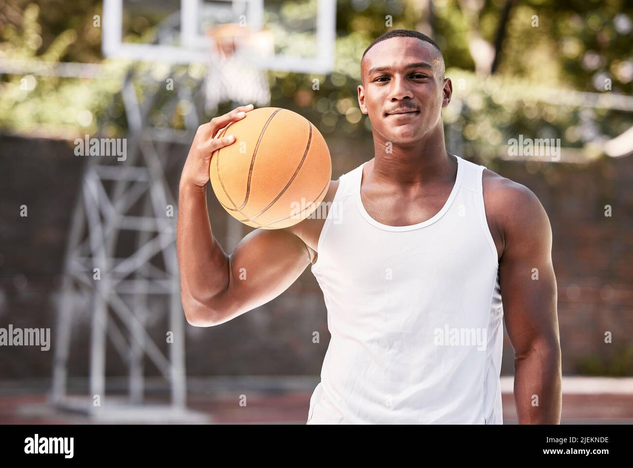 Portrait of a young black male basketball player holding a ball, playing a match on a local sports court outside. One cool muscular man with attitude Stock Photo