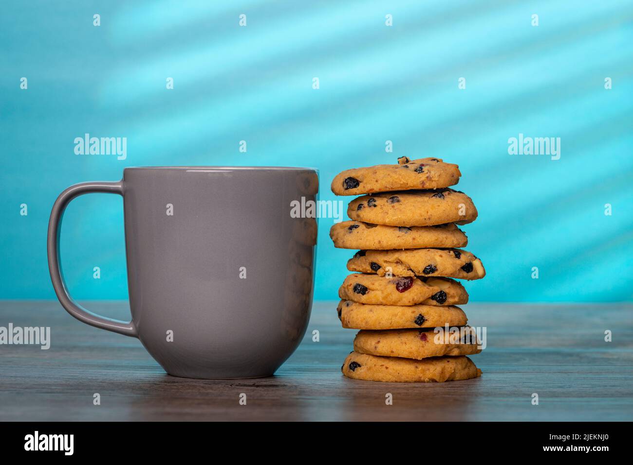 stack of home cooked cookies and a grey mug against a blue background Stock Photo