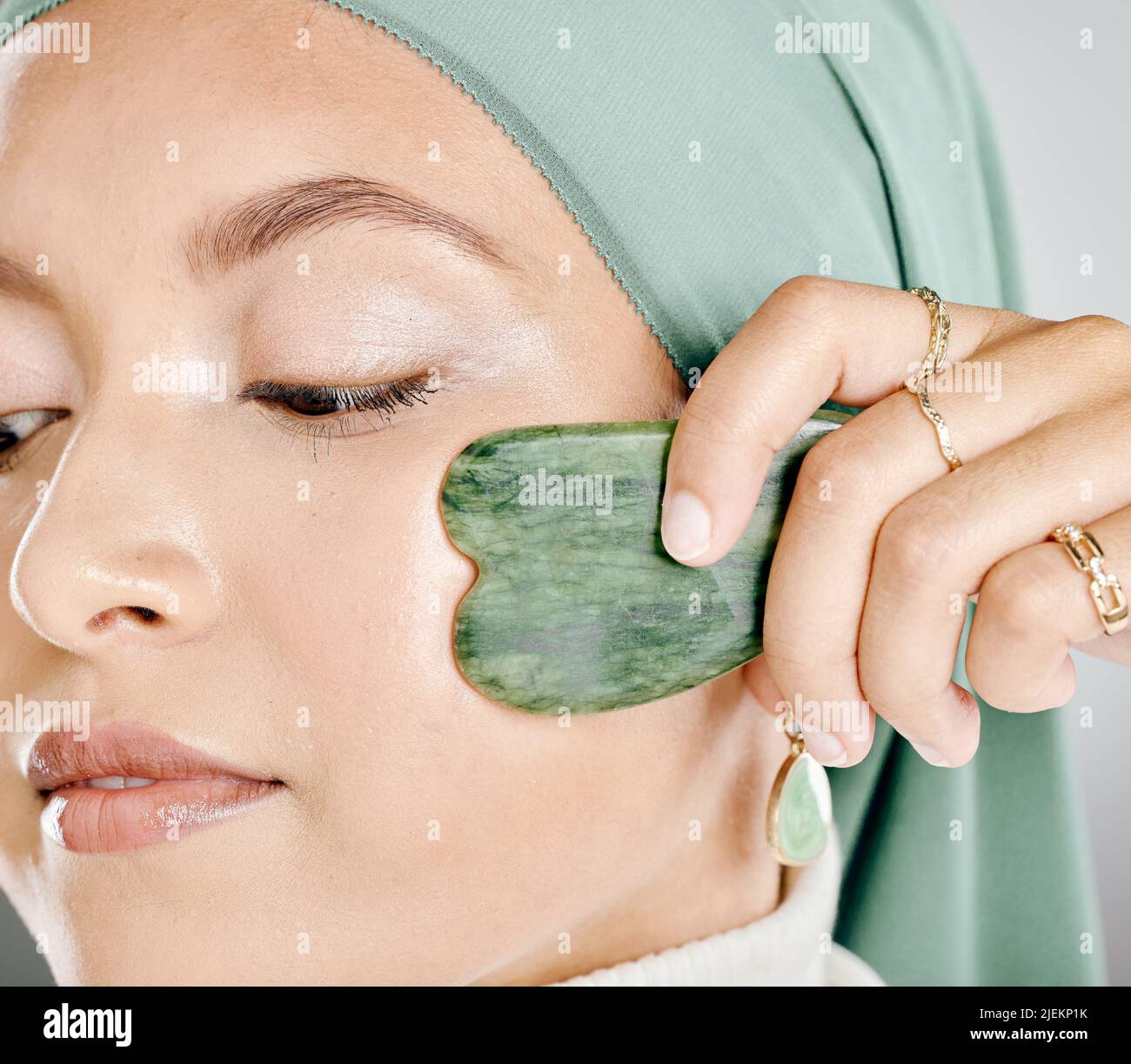 Muslim woman using a jade gua sha on face. Closeup headshot of an arab in a hijab sculpting face. Middle eastern woman using traditional chinese Stock Photo