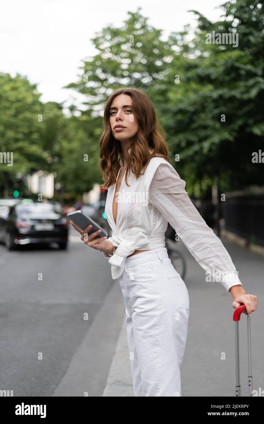 Trendy woman with mobile phone and suitcase on street in Paris Stock Photo