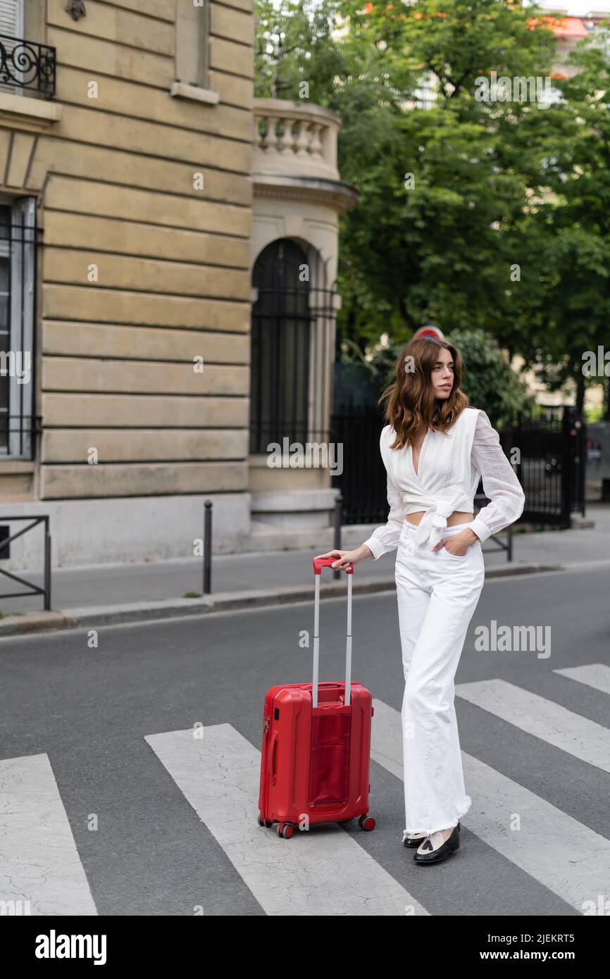 Trendy woman standing near suitcase on crosswalk in Paris Stock Photo