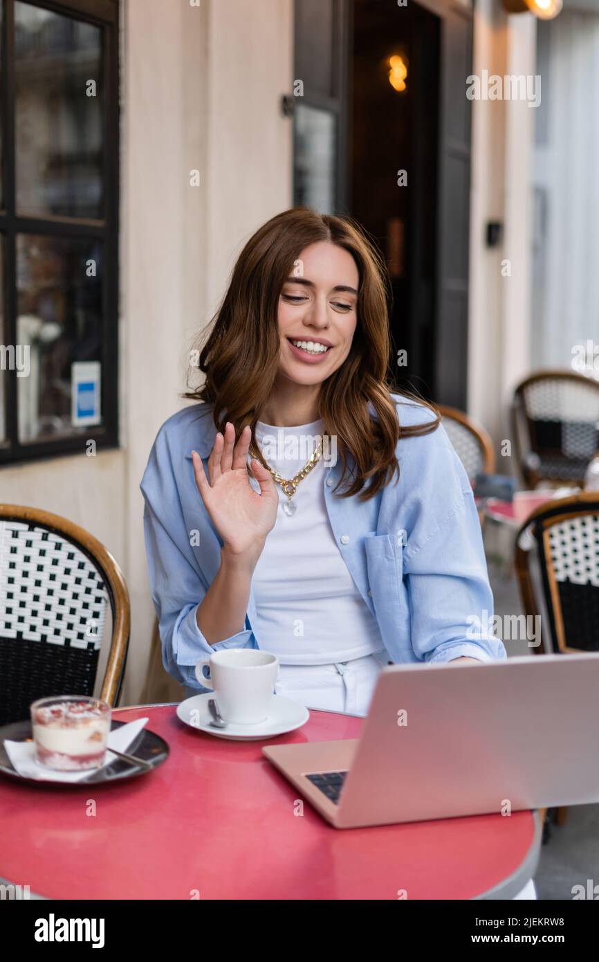 Stylish woman having video call on laptop near coffee and desert in