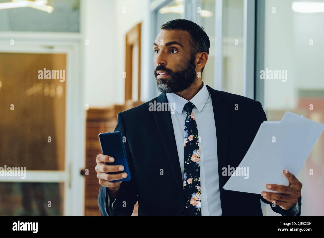 Mid adult bearded black man Entrepreneur Businessman wearing suit holding papers and smartphone walking in office shot Stock Photo