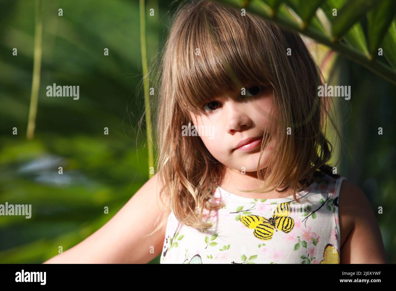 Cute European little girl sitting in the garden, close-up outdoor portrait Stock Photo