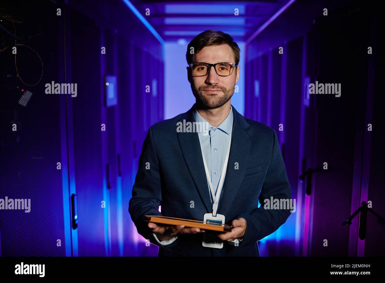 Waist up portrait of male network engineer holding tablet in server room and looking at camera Stock Photo