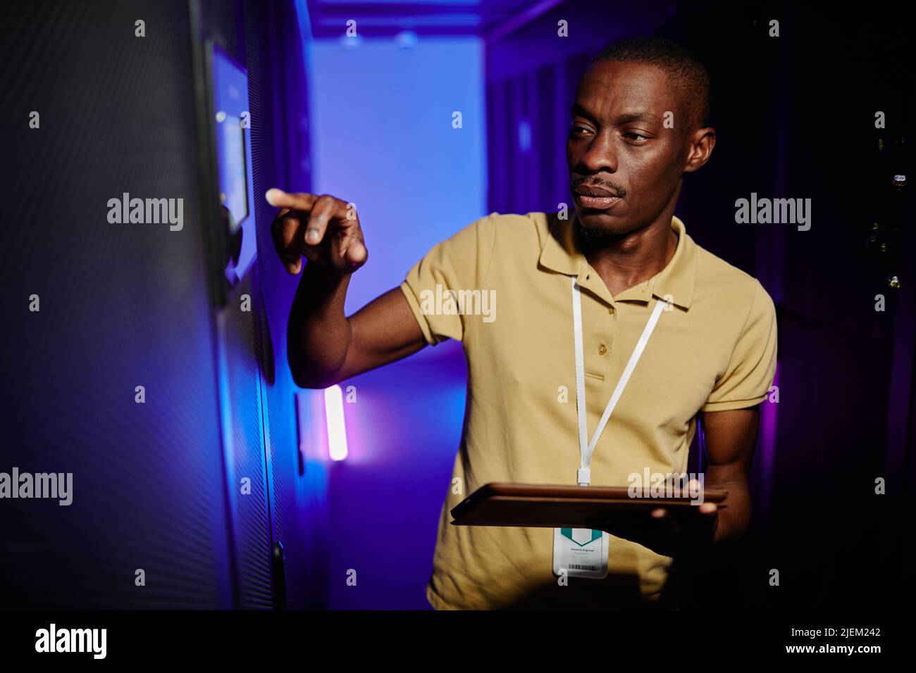 Waist up portrait of male system administrator setting up server network in data center lit by neon light Stock Photo