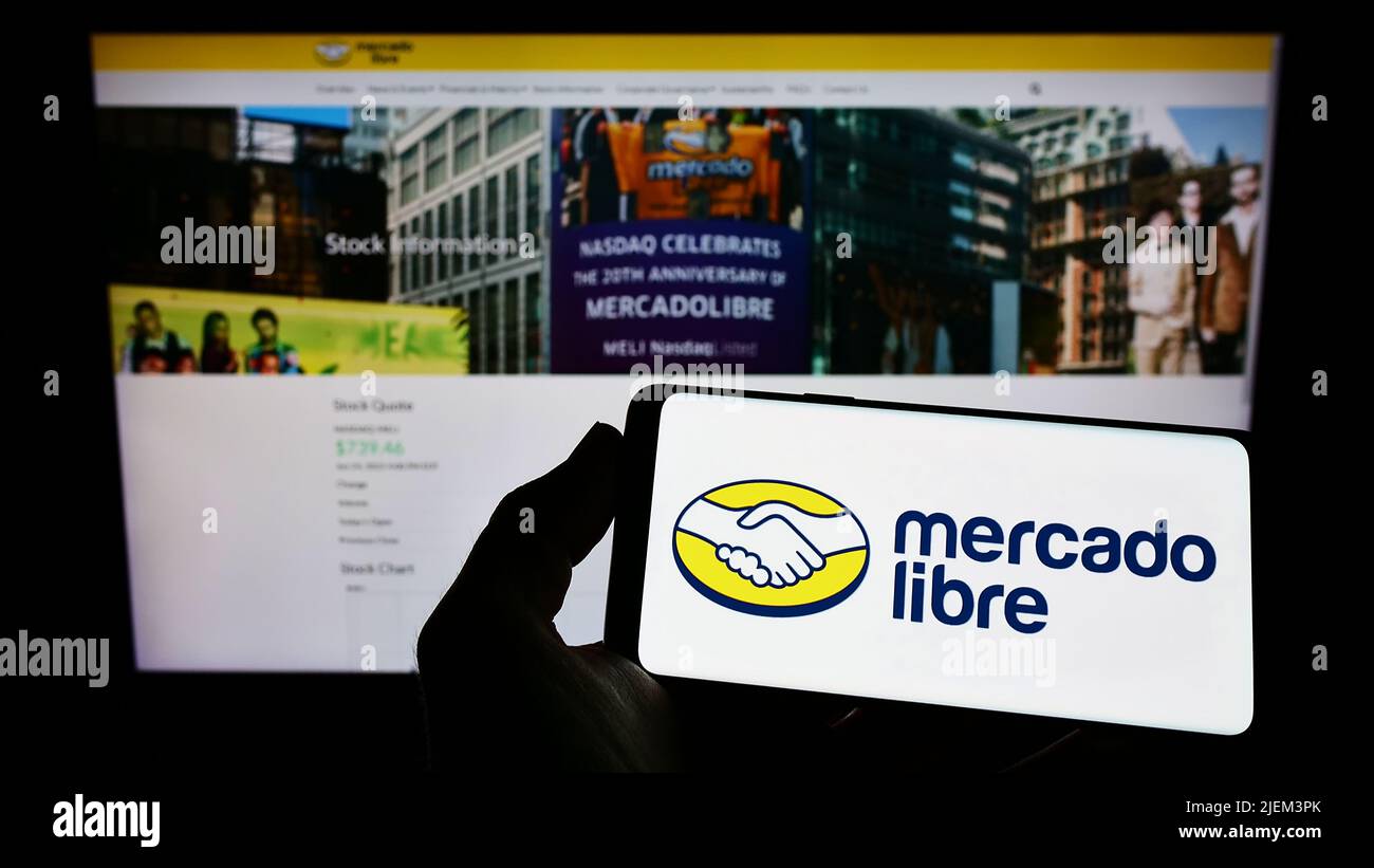 Person holding smartphone with logo of Argentine e-commerce company Mercado Libre Inc. on screen in front of website. Focus on phone display. Stock Photo