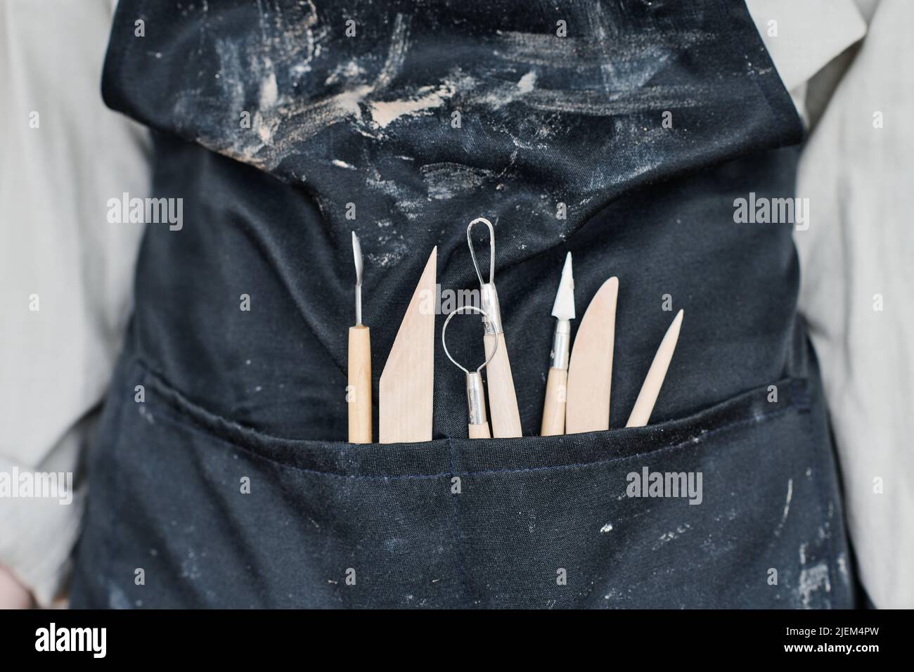 Part of craftsperson in black apron with handtools necessary for carving ornaments on handmade clay items in the front pocket Stock Photo