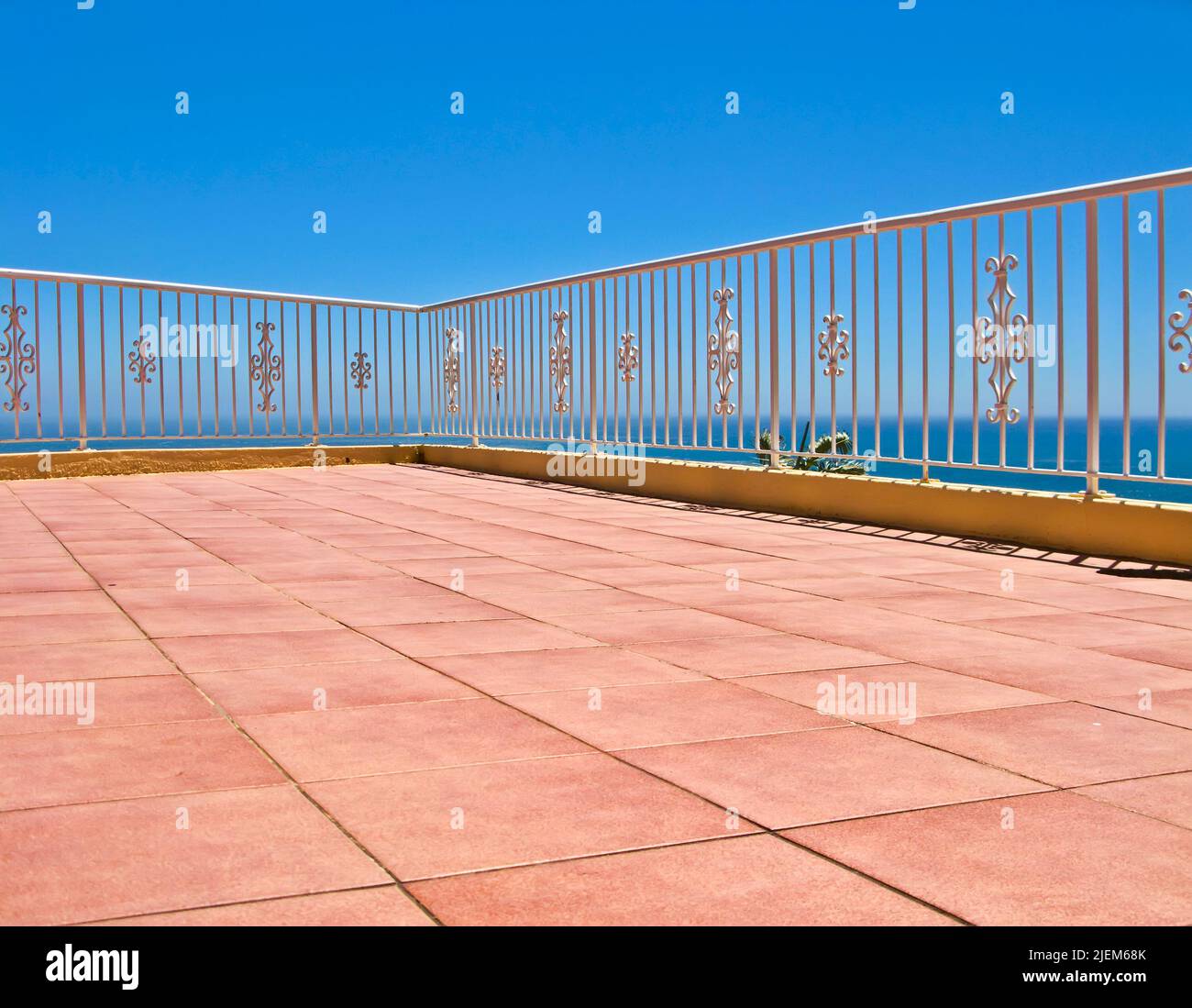 Beach house balcony or terrace with tiled floor and white fence. Summer view with a classic barricade overlooking the sea or ocean with a blue sky Stock Photo