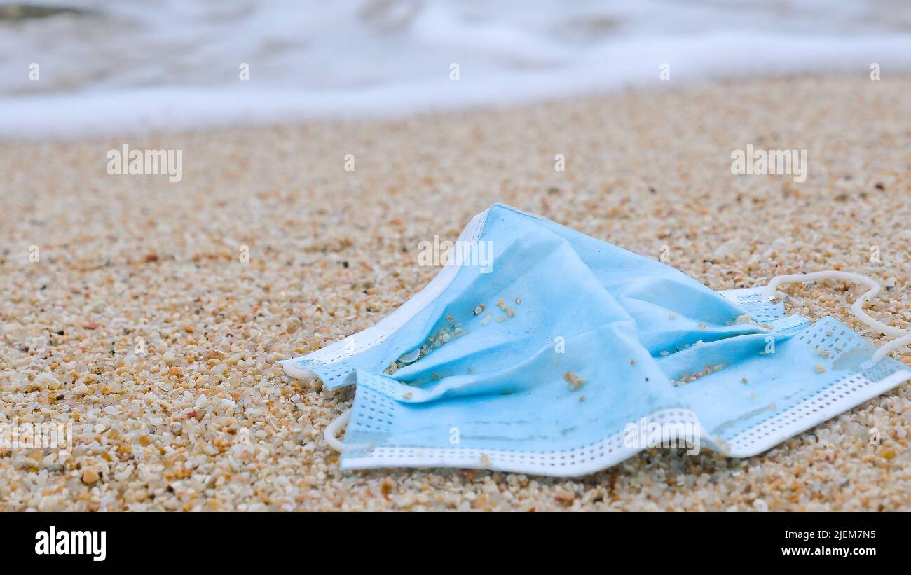 Coronavirus COVID-19 is contributing to pollution. Used face mask polluting tropical beaches. Polluted ocean coast with garbage. Environmental and Stock Photo