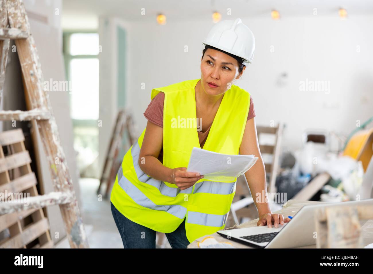 Woman builder checking project documentation and using laptop Stock Photo