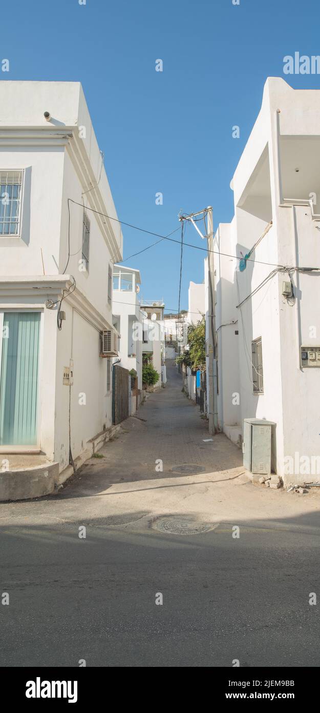Empty alley way in a rural tourist town surrounded by white houses or apartments. A narrow city street in Europe. A quiet road in an urban village Stock Photo