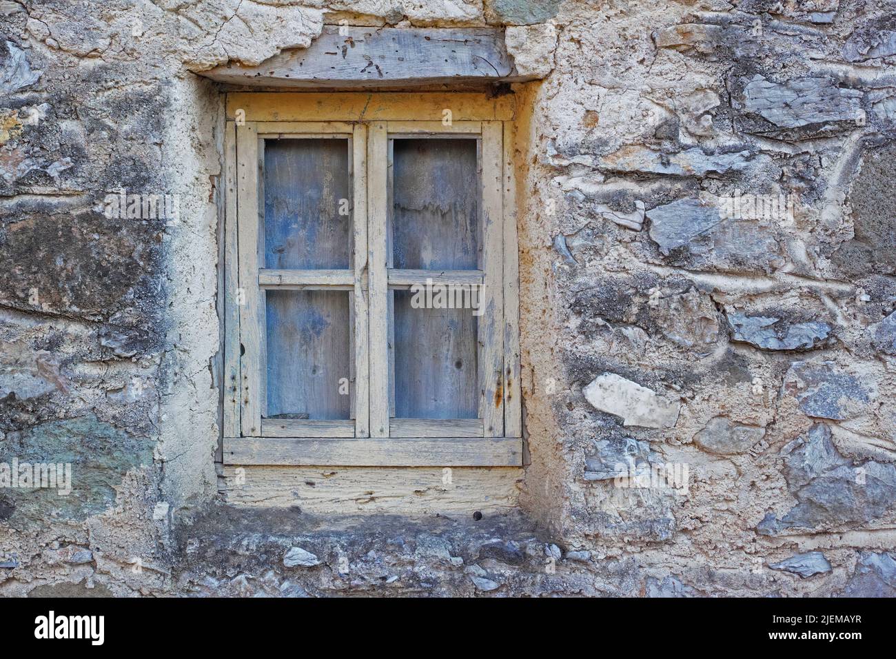 Closeup of a wooden window in a stone wall of an old grey house. Boarded up square window frame in a historic rustic building. Architecture and Stock Photo