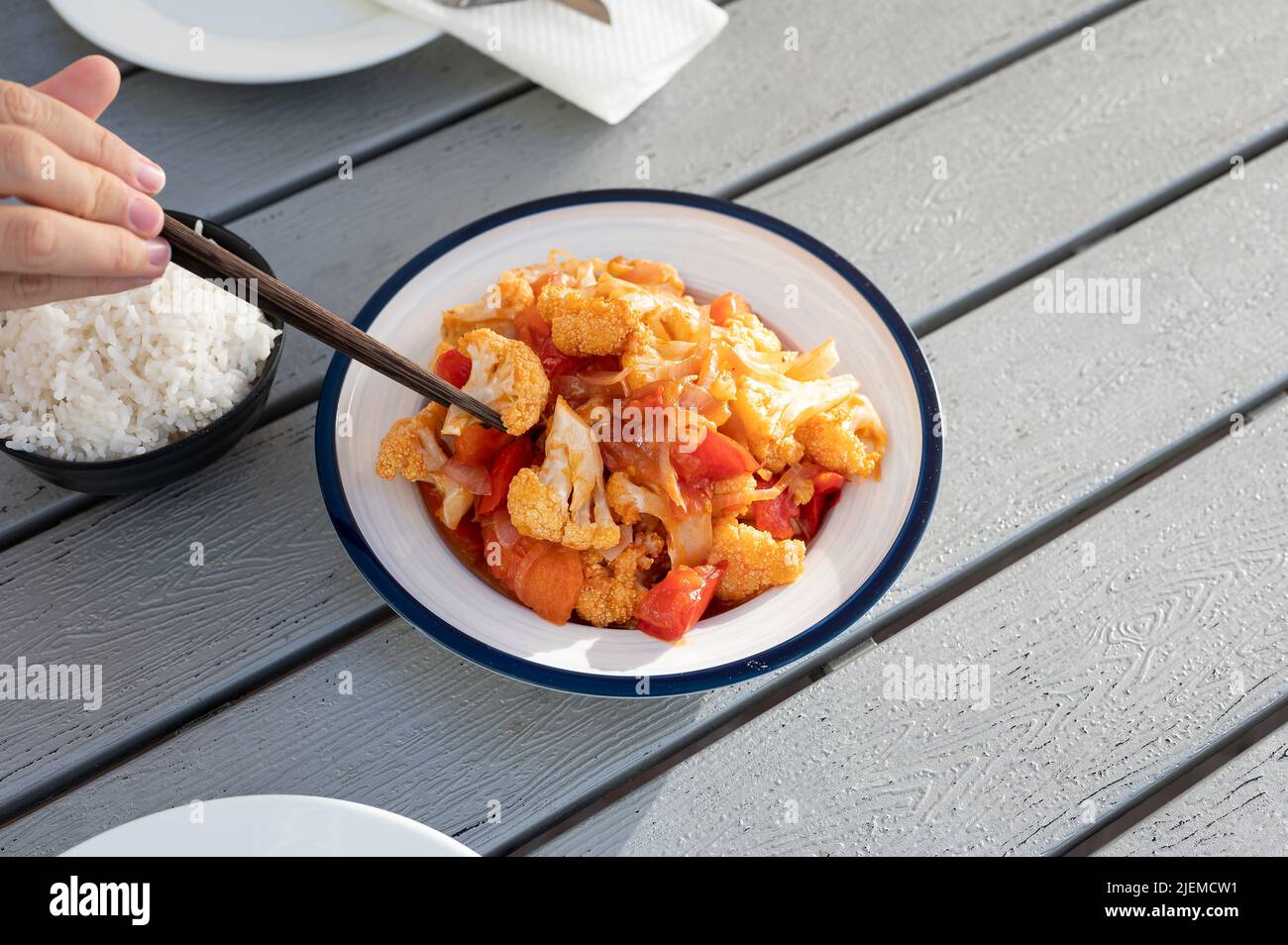 Woman eating spicy cauliflower with tomato and szechuan sauce with a chopstick.Chinese Asian food Stock Photo