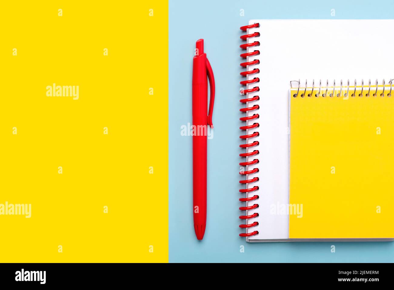 Top view of spiral notepad and red pen with space for text on blue and yellow background. Back to school concept Stock Photo