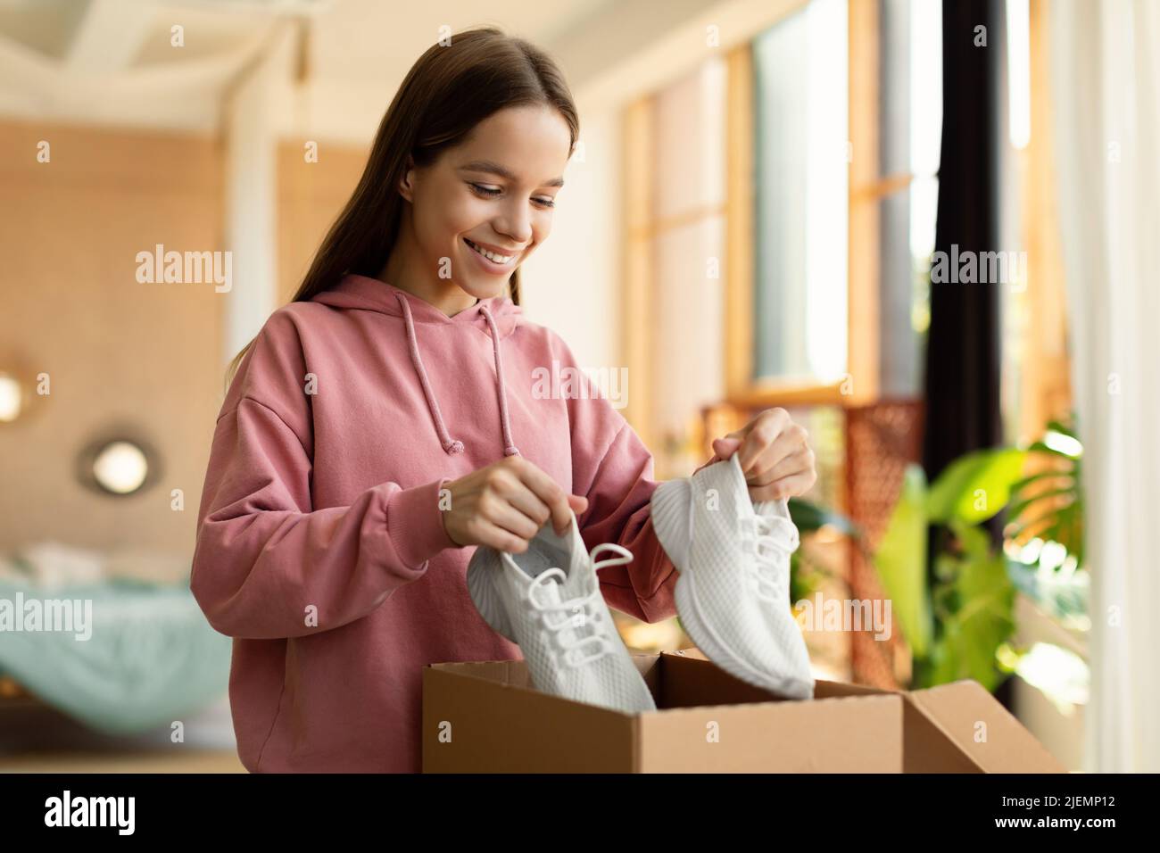 Happy teen girl buyer holding new footwear unpacking cardboard box, receiving shoes after