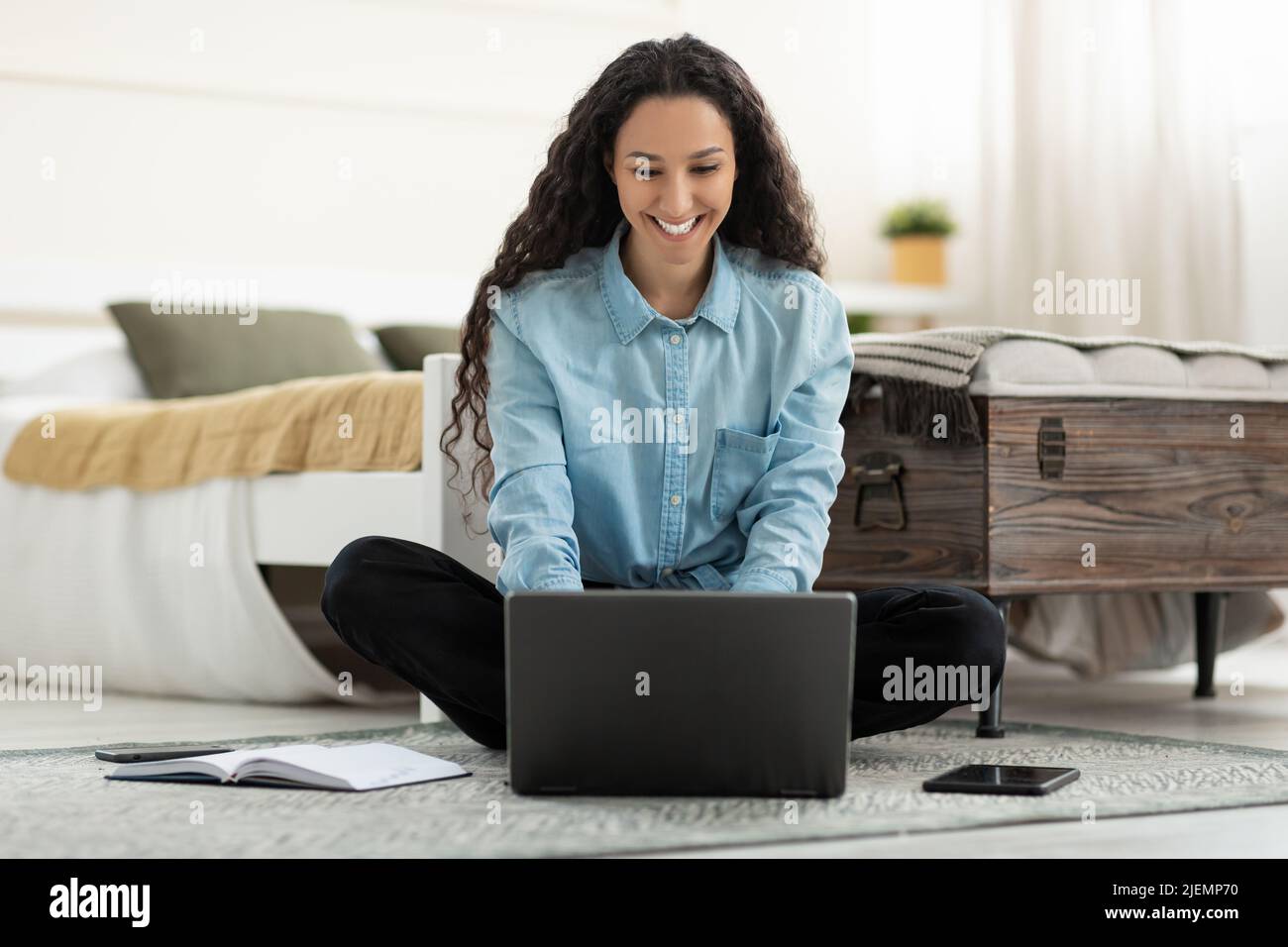 Beautiful young woman sitting on floor, working on laptop pc in bedroom ...