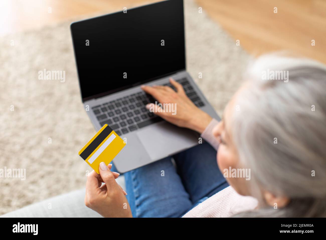 Cropped european senior woman with gray hair with credit card and laptop shopping online in room interior Stock Photo