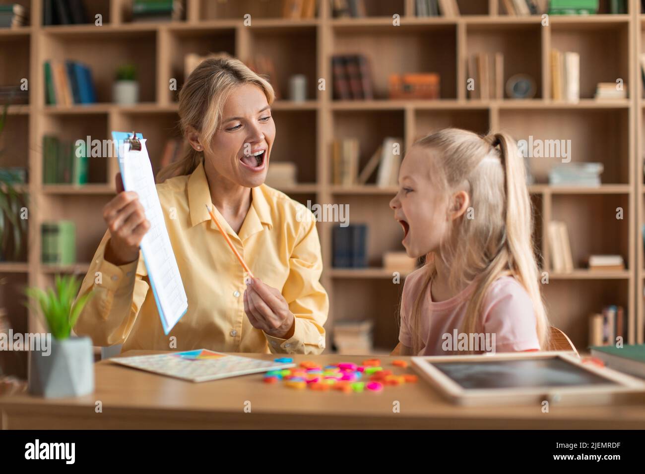 Cheerful female speech therapist curing child's problems and impediments, little girl learning letters during lesson Stock Photo