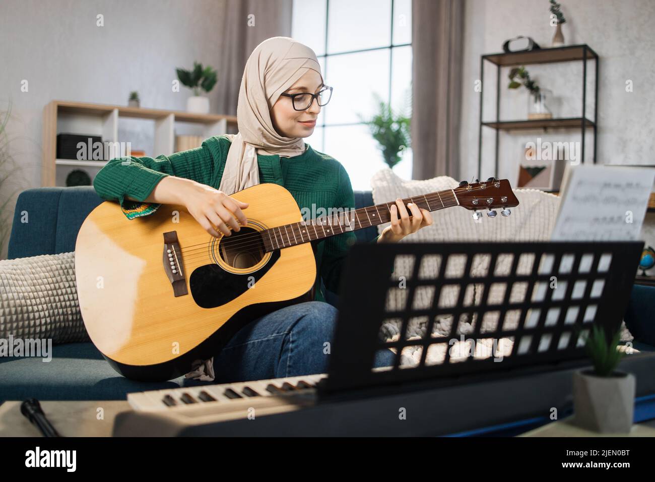 Young muslim woman in hijab plays guitar on bright living room at home ...