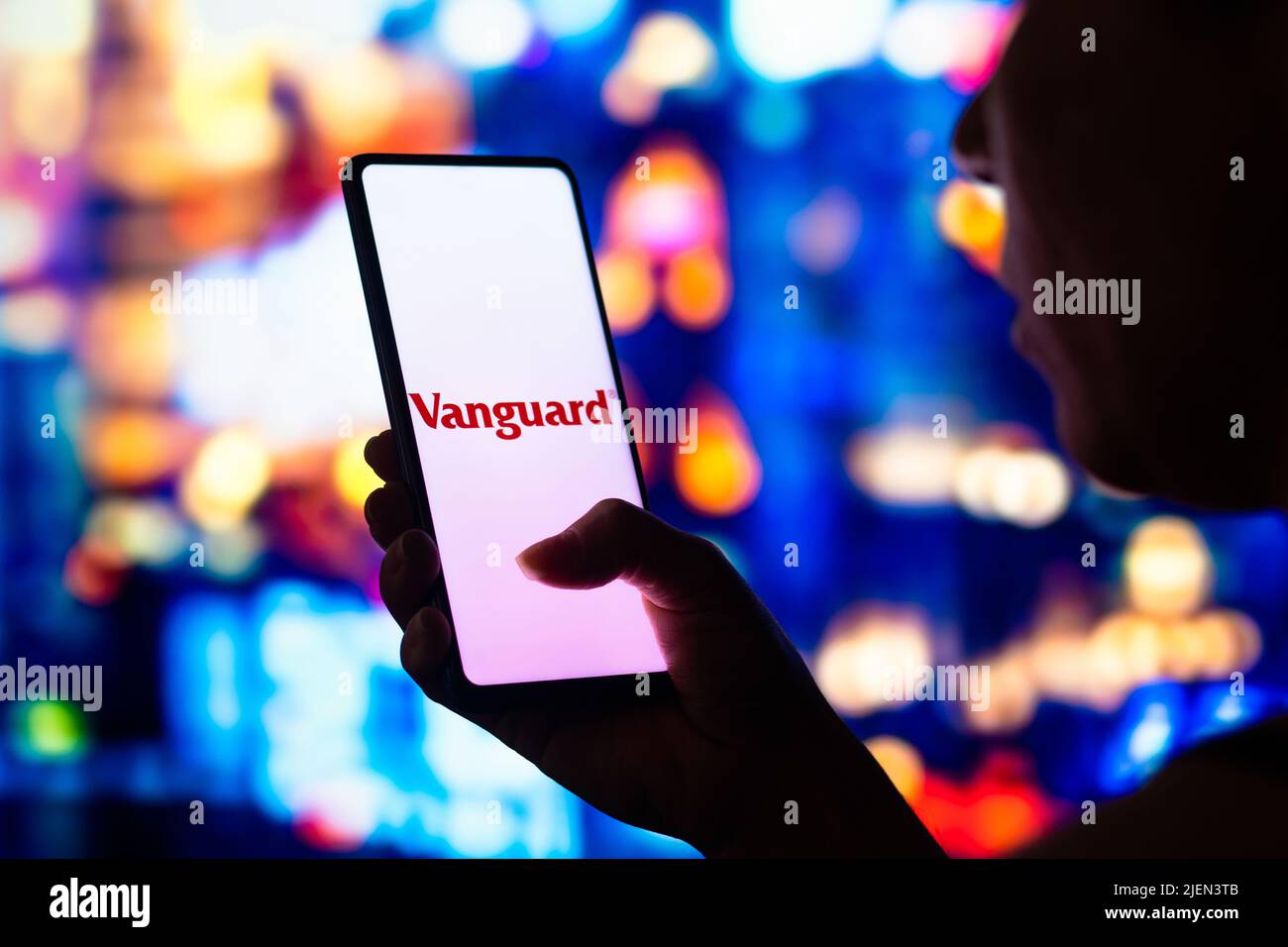 In this photo illustration, a silhouetted woman holds a smartphone with the Vanguard Group logo displayed on the screen. Stock Photo
