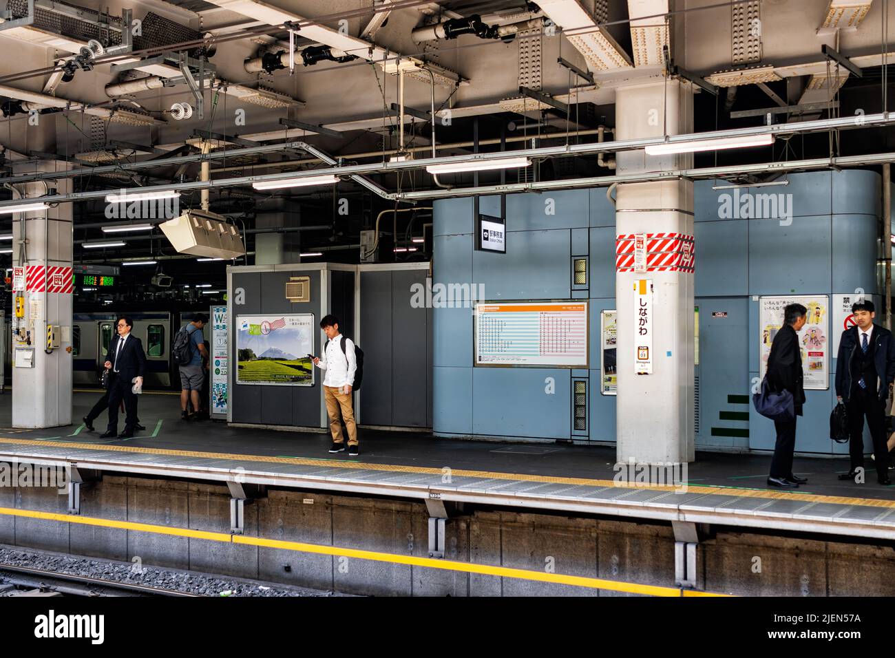 Shinagawa, Japan - April 17, 2019: Central train station platform with candid salaryman businessmen people waiting by tracks for JR shinkansen to arri Stock Photo