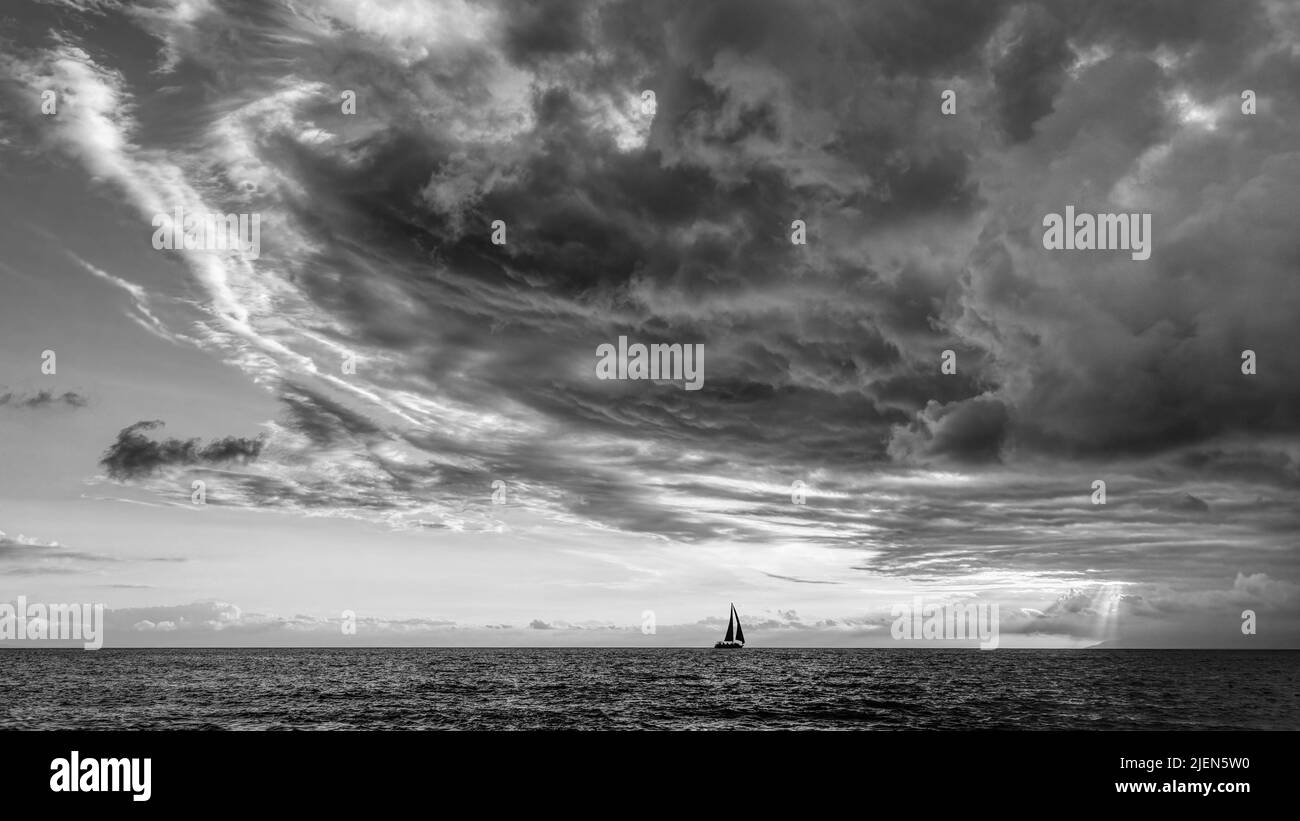 A Storm Is Looming Overhead As A Small Boat Moves Toward The Shining Light Black And White Stock Photo