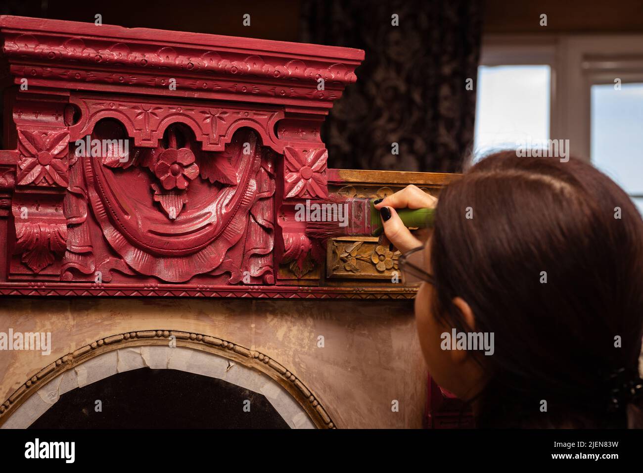 Woman painting upper part of ornamented wooden cupboard in pink with paint brush in hand. Giving new life to old things. Home furniture renovation Stock Photo