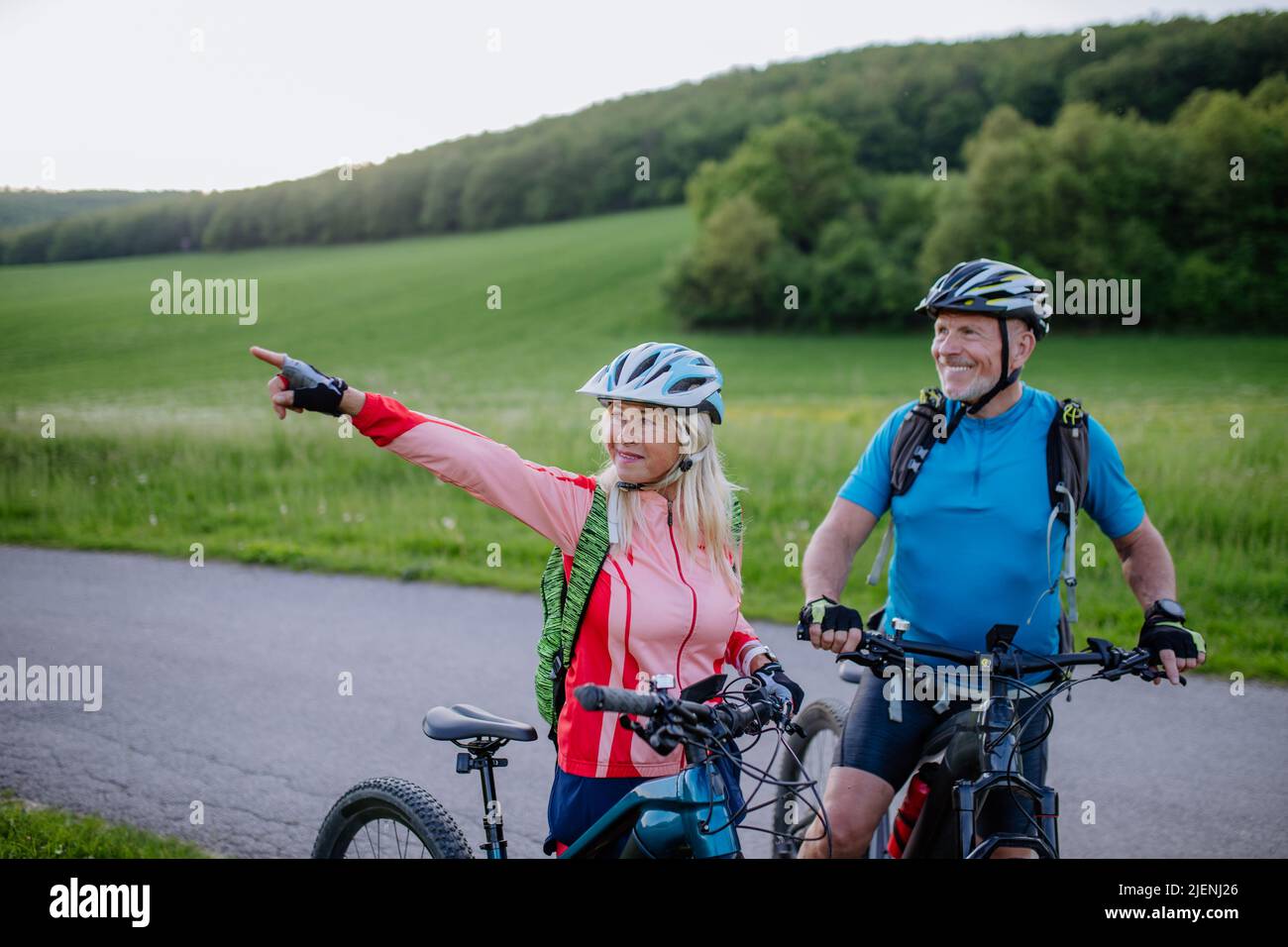 Active senior couple riding electric bicycles on road at summer park, healthy lifestyle concept. Stock Photo