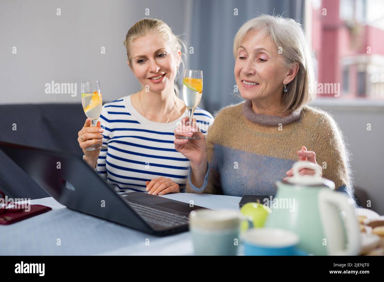 Elderly mother and adult daughter look at the laptop screen and congratulate relatives on the Internet on holiday Stock Photo