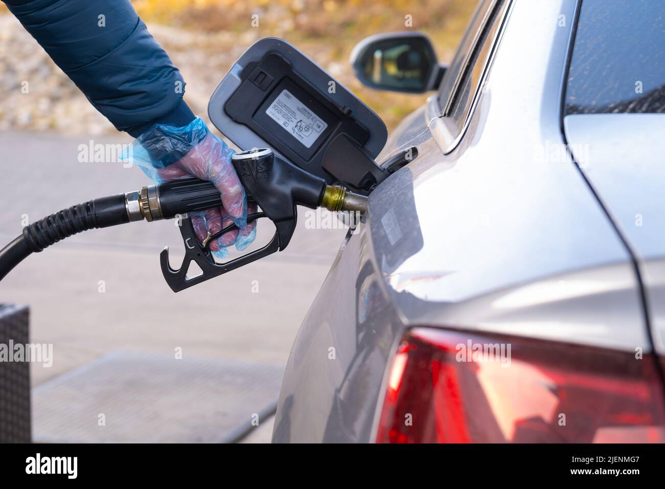 Fuel price in Europe. Refueling the car.Refueling pistol in the hands of a man in a glove.Car at a gas station. Silver car, refueling pistols and Stock Photo