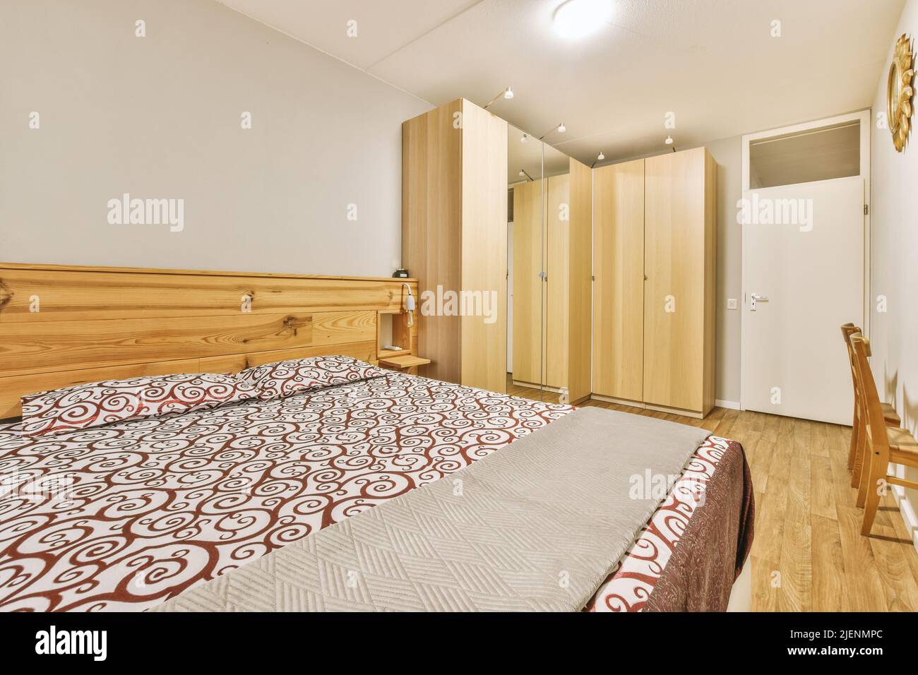 Comfortable bed with ornamental blanket placed and wardrobe with mirror in light bedroom Stock Photo