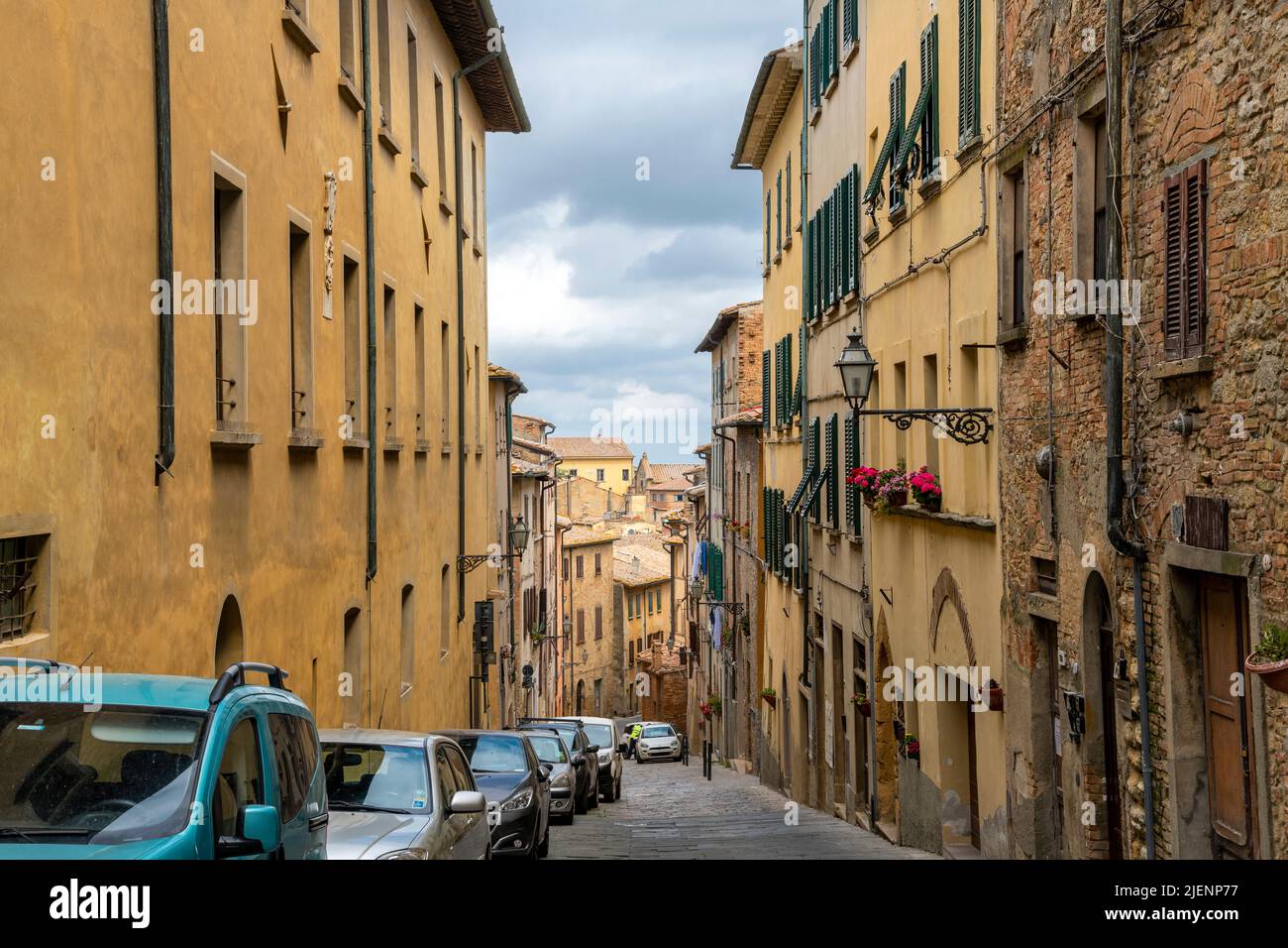 A picturesque sloping street with cars parked in the medieval center of the Tuscan hill town of Volterra, Italy. Stock Photo