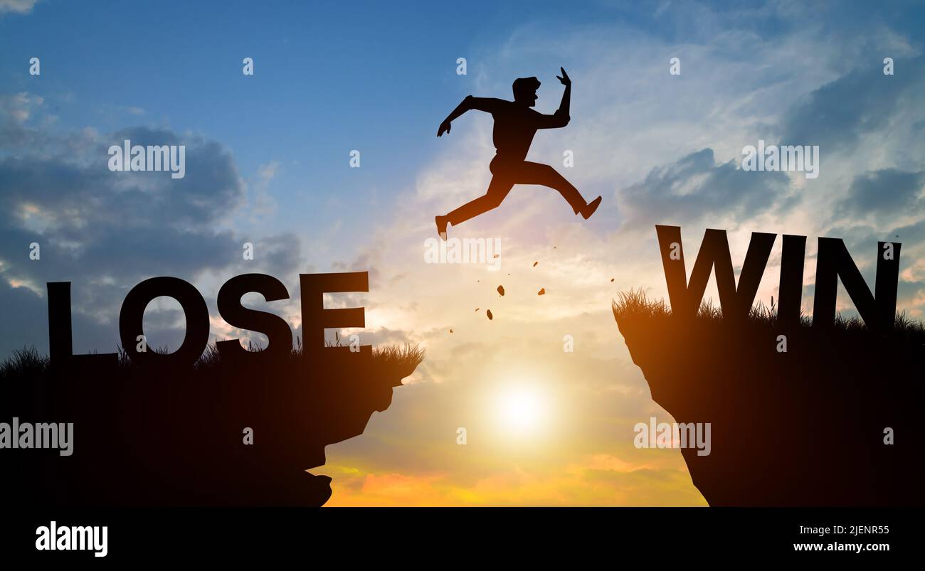 Silhouette man jumping from LOSE to WIN wording on cliffs with cloud sky and sunrise. Never give up and Business Concept. Stock Photo