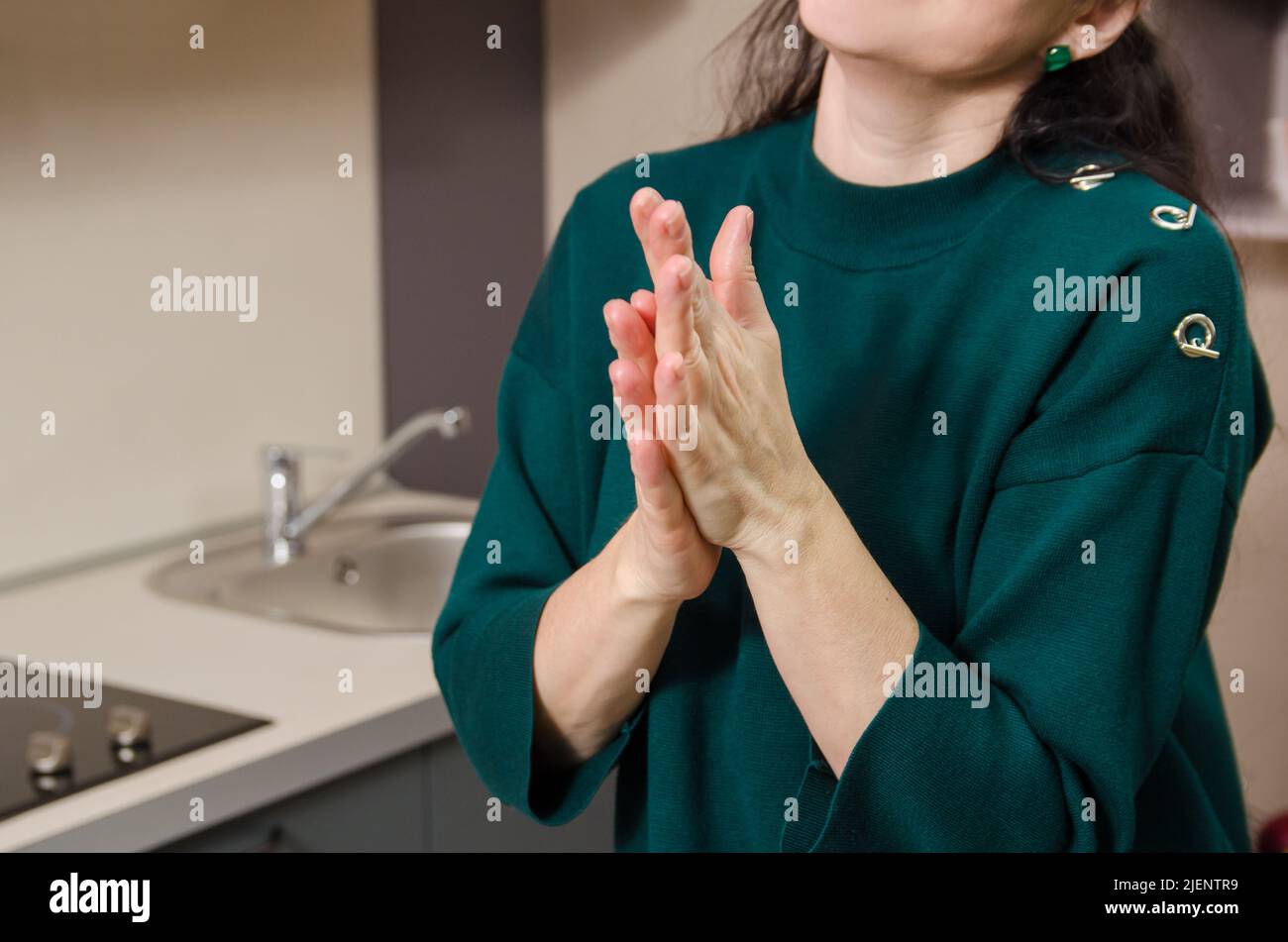 An unrecognizable woman applies cream to the palms of her hands after washing the dishes. Protecting and restoring the skin Stock Photo