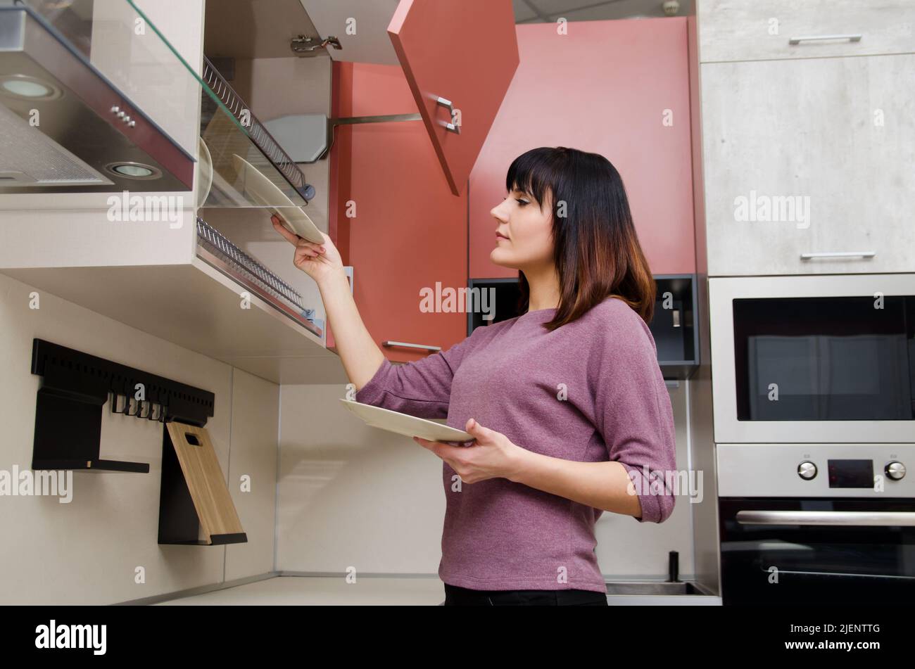 A young woman takes out a plate from the dish dryer in the kitchen Stock Photo