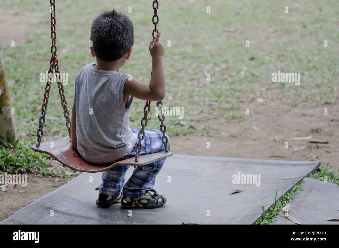 boy alone on a swing looking far, not showing his face only his back Stock Photo