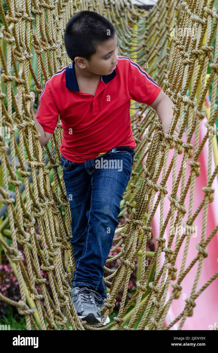 Boy wearing pink looking at his left side in the middle of a net of ropes Stock Photo