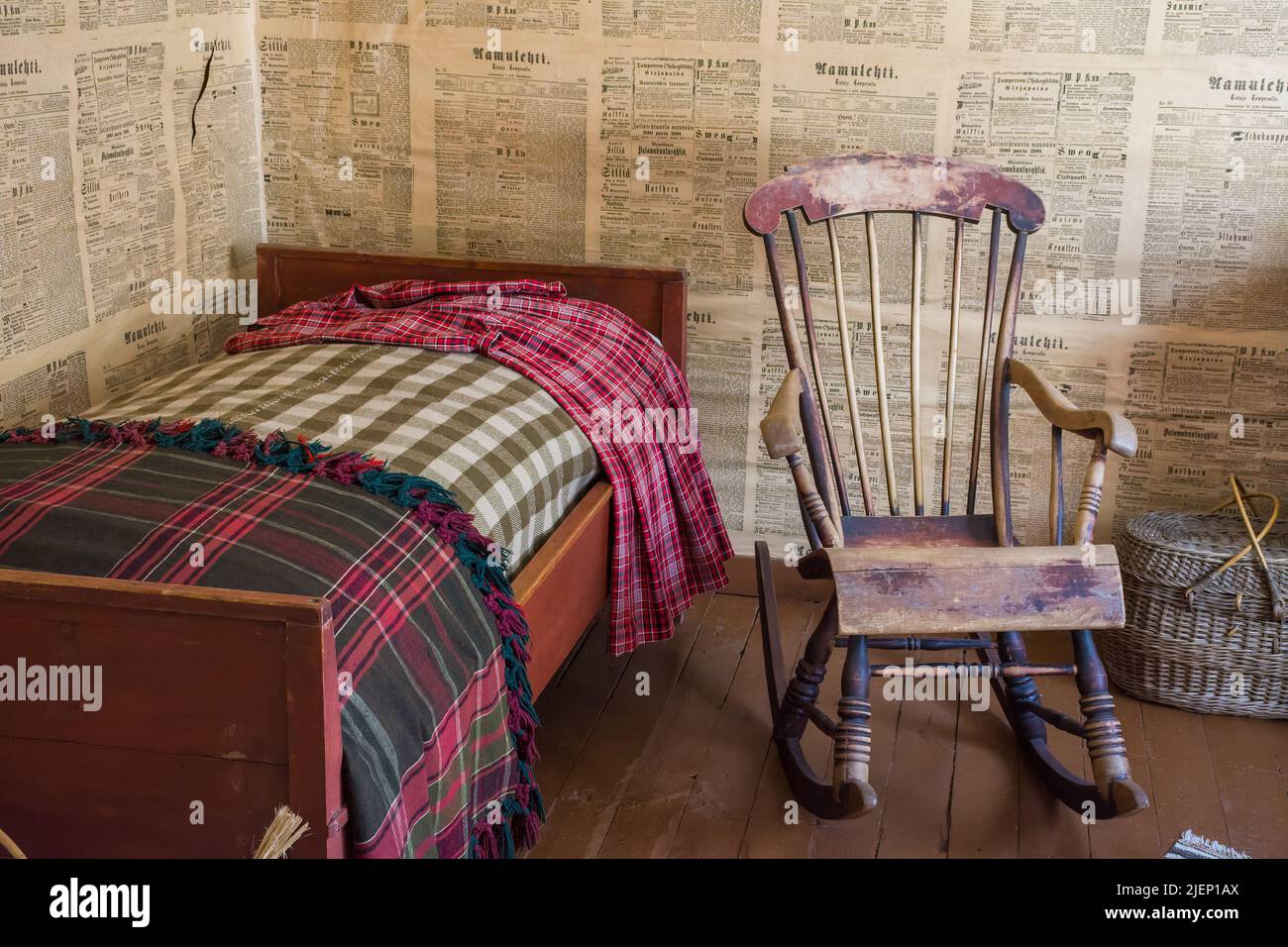 Bed and rocking chair in a room with newspaper as wall papers on log wall at Amuri Museum of historic Housing in Tampere Finland Stock Photo