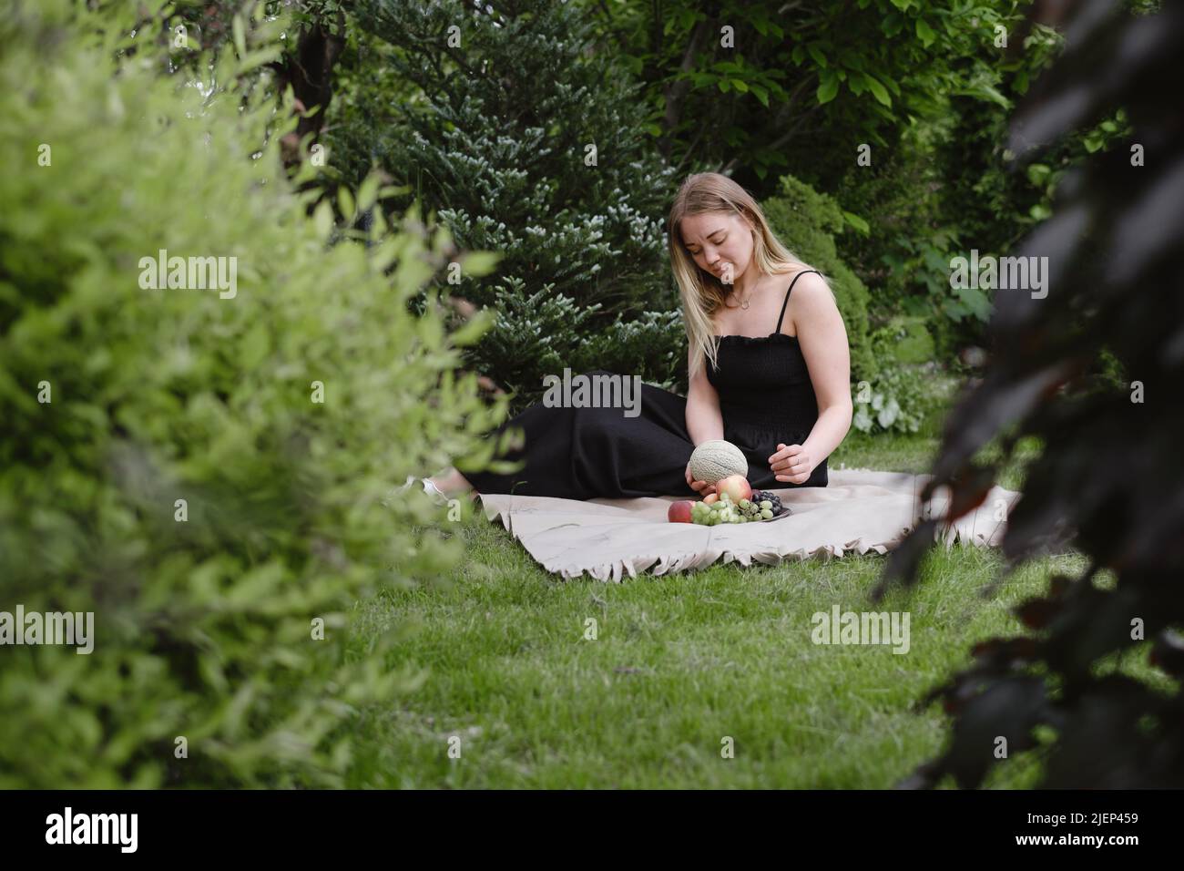 Woman on picnic in green garden On blanket. Cheerfully female spend time outdoors, eating summer fruits. Vegetarian eco idea for weekend picnic Stock Photo