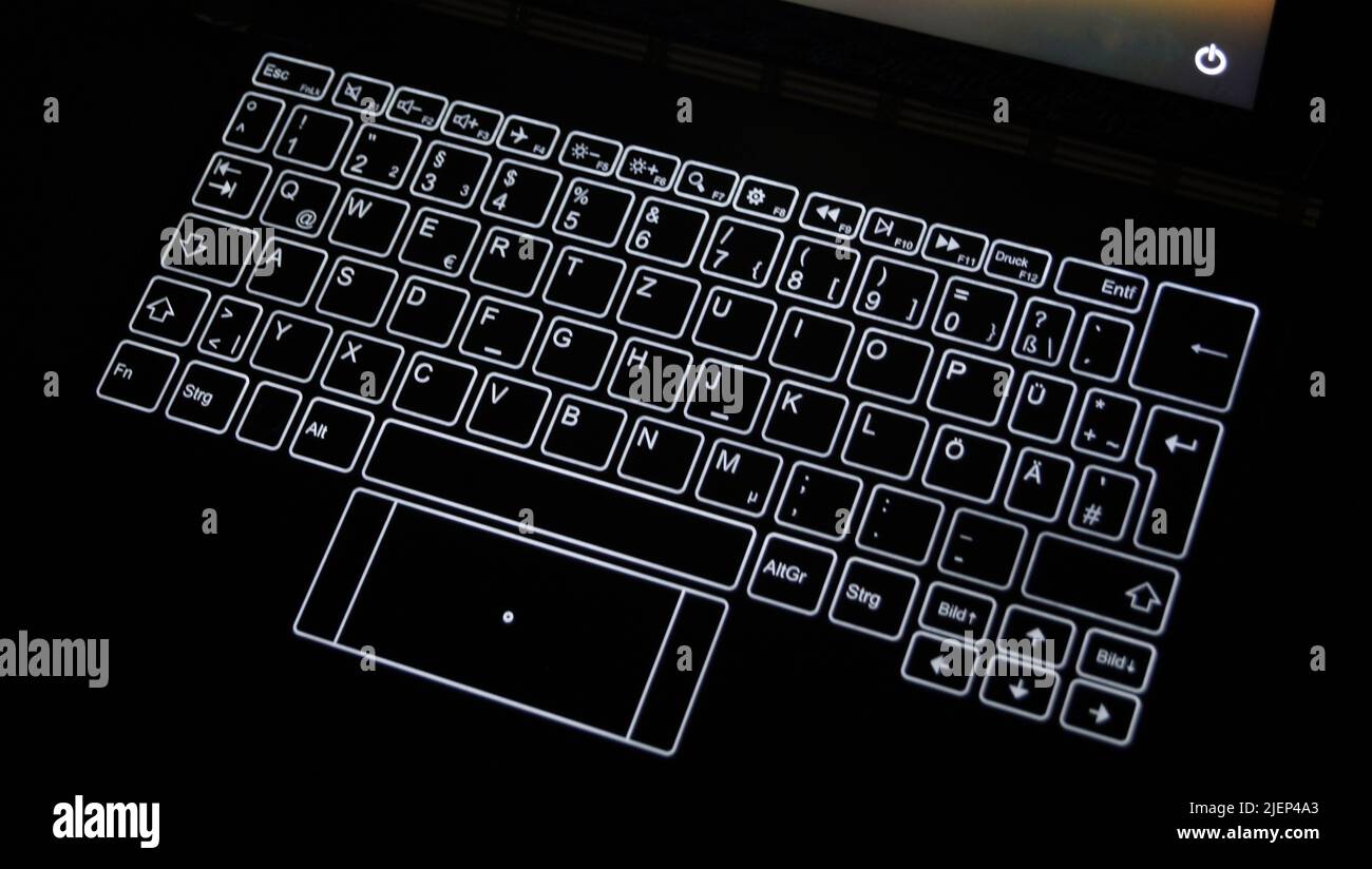 Detail of a notebook with glowing keys in the dark. The power-off symbol on a screen is shown in right top of the photo Stock Photo