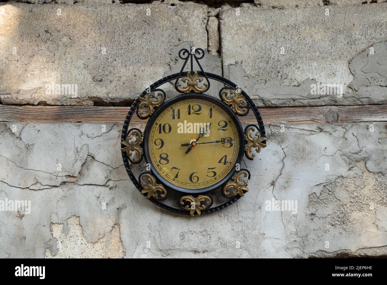 old broken clock ussr hangs on the white wall of a house in the street in the sun, broken old