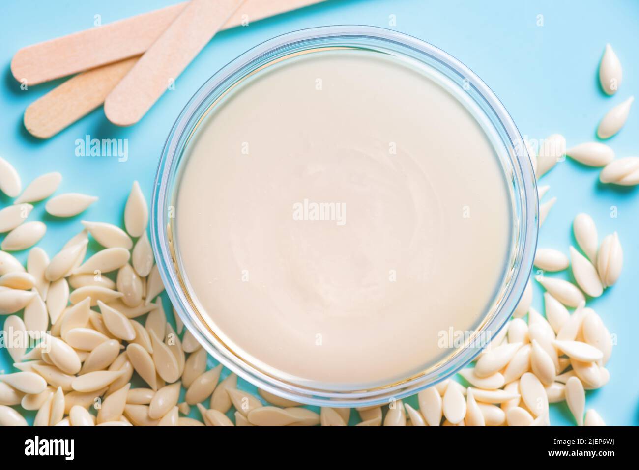 Natural depilatory melted wax and  film wax bean granules on blue background close up. Hair removal, natural beauty concept,  pearl wax. Stock Photo