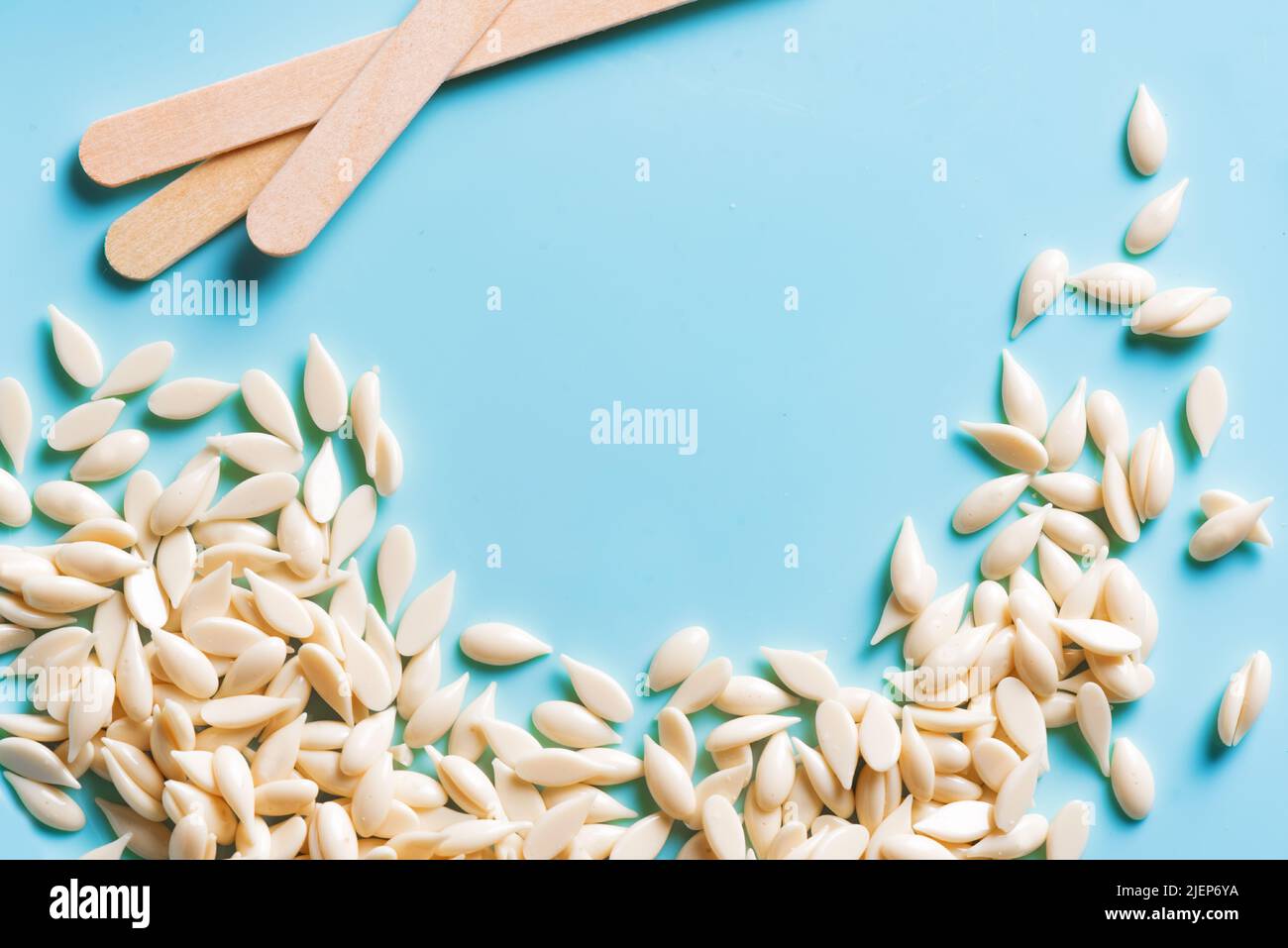 Natural depilatory film wax bean granules and wooden spatula on blue background close up. Hair removal, natural beauty concept,  pearl wax. Stock Photo